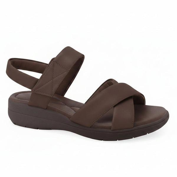 A dark brown wedge sandal with criss-cross straps and an adjustable ankle strap, shown from a side profile on a white background. A 'Genuine Leather' badge is visible in the top right corner.