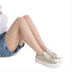 Person wearing gold carmela sneakers with white laces on a white background