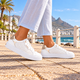 Carmela white floral leather sneakers worn on a seaside promenade